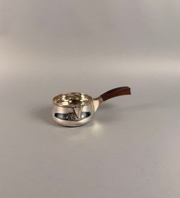 une casserole en argent avec un manche en bois posée sur une surface blanche