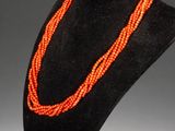 an orange beaded necklace is displayed on a black mannequin