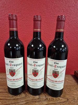 trois bouteilles de vin rouge sont posées sur une table devant un mur rouge