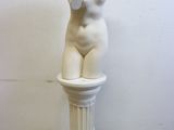 sculpture représentant un torse féminin posée sur un socle devant un mur blanc