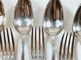 five silver spoons and two silver spoons on a white table
