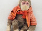 un singe en peluche portant une veste orange, assis sur une surface blanche