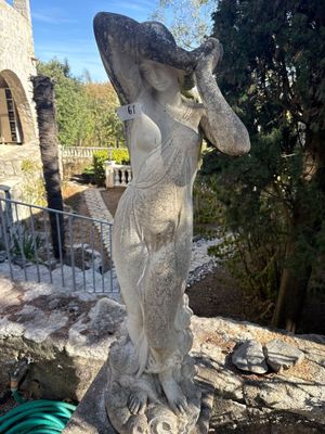 une statue représentant une femme tenant un chapeau, au sommet d'un mur de pierre
