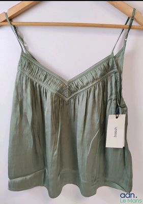 the top of a women ' s green top hangs on a hanger