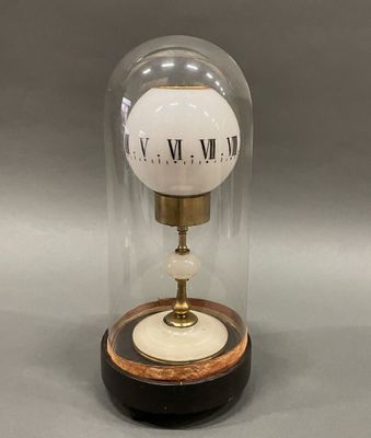 clock in a glass dome on a wooden base on a gray surface