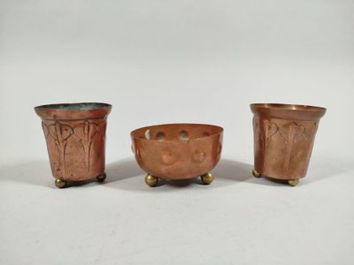 three small copper pots with handles on wheels on a white surface
