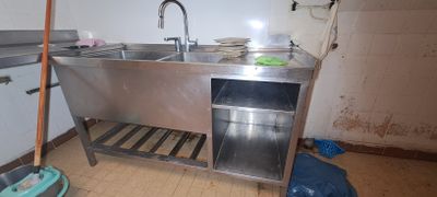 a stainless steel sink in a dirty kitchen next to a trash can