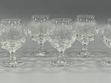 six clear wine glasses lined up in a row on a white surface