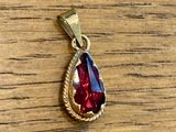 un pendentif rouge et or en forme de larme posé sur une table en bois