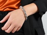 une femme vêtue d'un blazer noir et d'un haut orange, tenant un bracelet à chaîne argentée