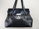 sac à main en cuir noir accroché à un mur, avec un mur blanc en arrière-plan