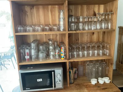 a wooden shelf with many glasses and a microwave on it