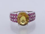 a close up of a ring with a yellow topazr surrounded by pink sapphires
