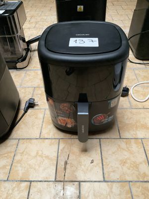 une friteuse à air chaud noire et argentée posée sur un sol carrelé