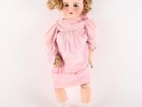 poupée aux cheveux blonds, vêtue d'une robe rose et de chaussures blanches, sur fond blanc