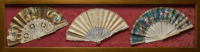 trois éventails en papier disposés en forme d'éventail dans un cadre en bois sur fond rouge