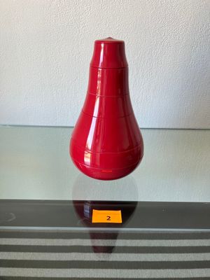 un vase rouge posé sur une table en verre, avec une étiquette jaune