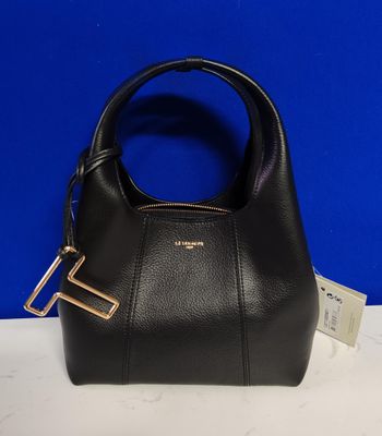 un sac à main noir muni d'une poignée métallique posé sur une table blanche