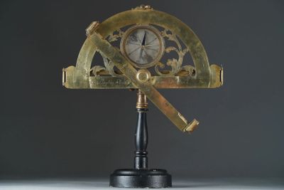 un compas doré posé sur un socle noir, sur lequel se trouve une horloge dorée