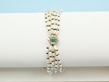 a close up of a white napkin with a silver and green beaded bracelet