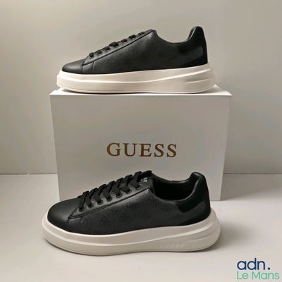 des baskets en cuir noir à semelles blanches exposées devant une boîte blanche