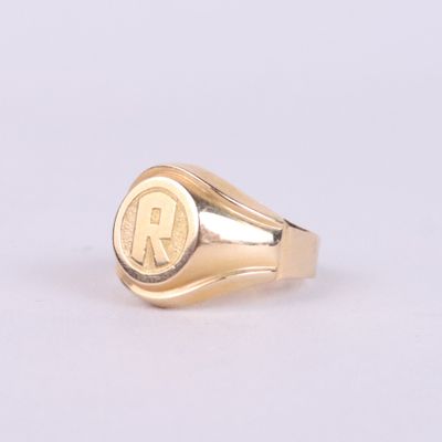 une image représentant une bague chevalière en or sur laquelle figure la lettre « r »