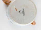 une tasse blanche avec une anse marron posée sur une surface blanche