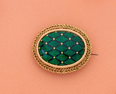 une image représentant une broche verte et dorée posée sur un fond rose