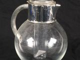a clear glass pitcher with a silver lid on a black background