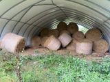 Des balles de foin sont empilées dans un abri métallique, dans un champ