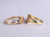 two gold rings with pink and yellow stones on a white surface