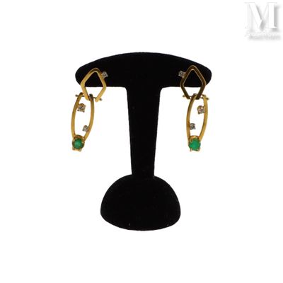 une paire de boucles d'oreilles en or et émeraude posée sur un socle noir