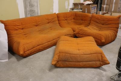 un grand canapé orange et un pouf dans une pièce