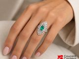 woman ' s hand with a diamond and emerald ring sitting on a couch