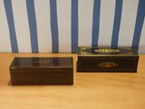 pair of black and gold boxes on a wooden table with blue and white striped wallpaper