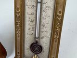 a gold frame with a thermometer on it next to a wooden spoon