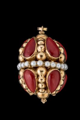 un gros plan sur une broche dorée et rouge ornée de perles