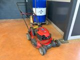 a red lawn mower sitting on the floor next to a blue barrel