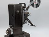 un vieux projecteur de cinéma posé sur une table, à côté d'une bobine