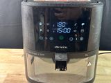 an air fryer sitting on top of a wooden table next to a black curtain