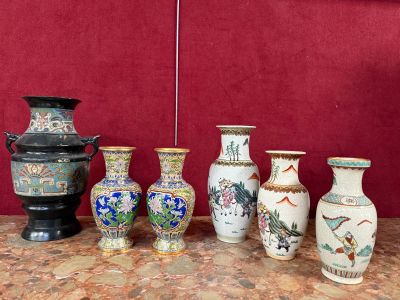 Plusieurs vases sont alignés sur une table, avec un mur rouge en arrière-plan.