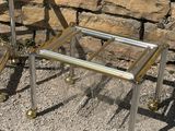 pair of chrome and glass side tables on wheels in front of a stone wall