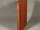 un livre orange à la couverture dorée posé sur une surface grise
