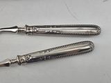 pair of silver plated knives on a white surface with a knife in the middle