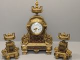 une horloge en or et trois bougies posées sur une table