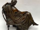 statue en bronze représentant une femme assise sur une chaise, le bras posé sur un coussin