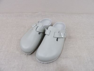 une paire de sabots blancs à boucles posée sur une surface blanche