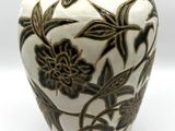 un vase blanc orné de fleurs noires, posé sur un fond blanc