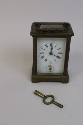 une petite horloge et une clé posées sur une surface blanche