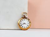 gold pocket watch with roman numerals sitting on a marble block